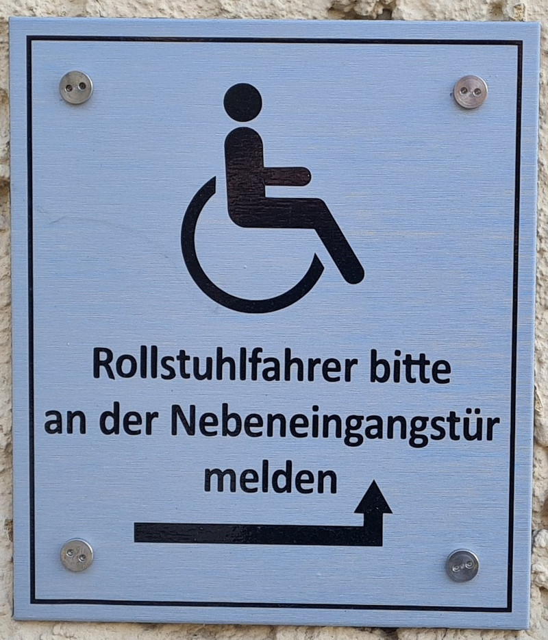 Hinweisschild Haupteingang Hinweisschild am Haupteingang das auf den Rollstuhlgerechten Eingang an der Seite des Amtsgerichts verweist